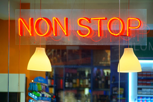 Close up view of a shop window neon sign of a non stop working market.