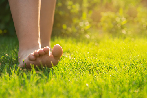 Teenage girl walking barefoot on green grass outdoors, closeup. Space for text