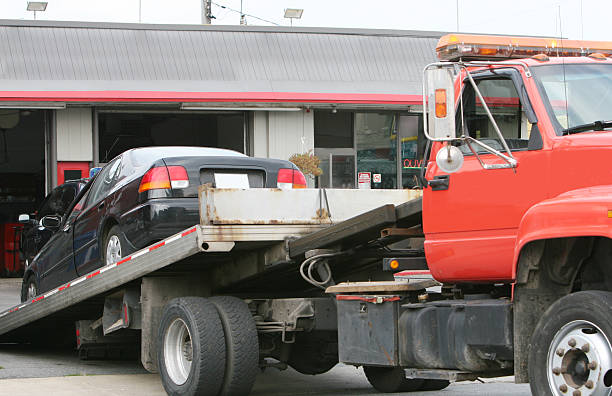 Black car on a red flat bed tow truck Tow truck bringing a car at the car repair shop. towing photos stock pictures, royalty-free photos & images