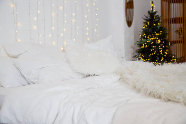 istock Christmas decorated bedroom interior with comfortable bed, Christmas fir tree and gift boxes on floor, copy space. Cozy home moment. Happy New Year. christmas garland lights at home 1722877105