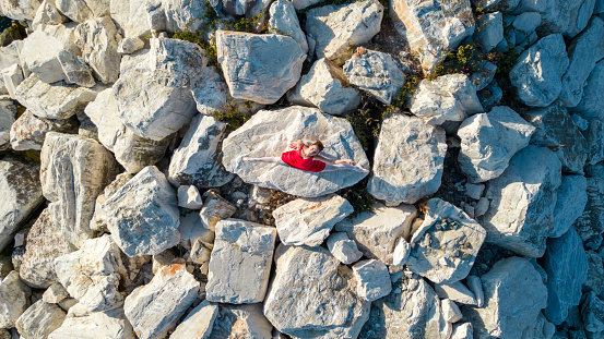 Ballerina dancing on the rocks in her red dress. Drone shooting.