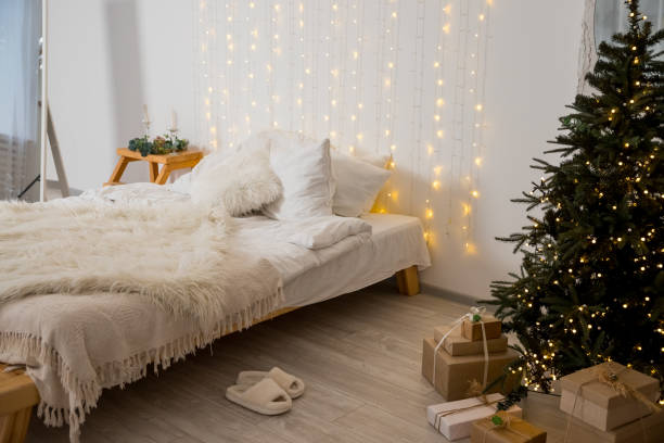 istock Christmas decorated bedroom interior with comfortable bed, Christmas fir tree and gift boxes on floor, copy space. Cozy home moment. Happy New Year. christmas garland lights at home 1722878673