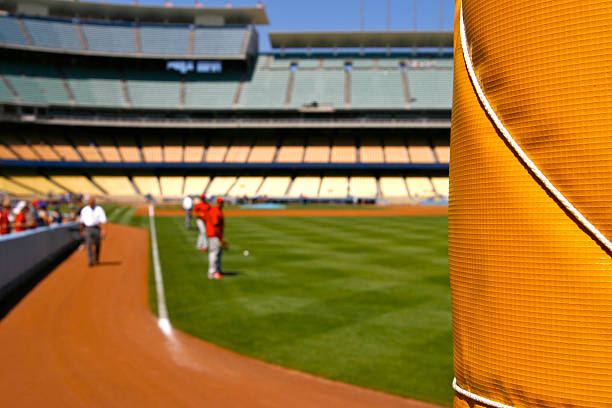 Focus on padded right field foul pole fence in foreground with baseball players exercising in unnumbered warmup jerseys in the background at a baseball stadium before the game