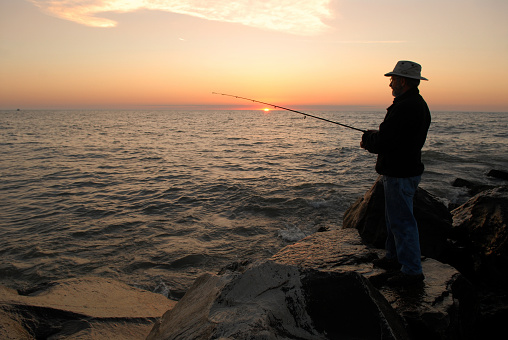 Fisherman silhouette in front of an early morning sunrise sky fishing out of his boat during a summer sunrise on lake