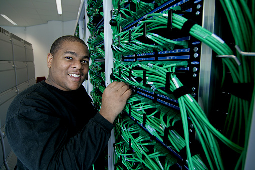 An IT Guy plugges in some ethernet cables in the server room.