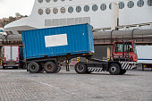 Specific truck for unloading ferry trailers, equipped with a lifting fifth wheel and automatic release, transporting a container.