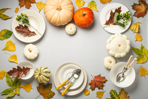 istock Thanksgiving festive table composition with different colourful pumpkins, autumn leaves, empty plates with cutlery on light grey background table ready for party and celebration. Space for text 1722895639