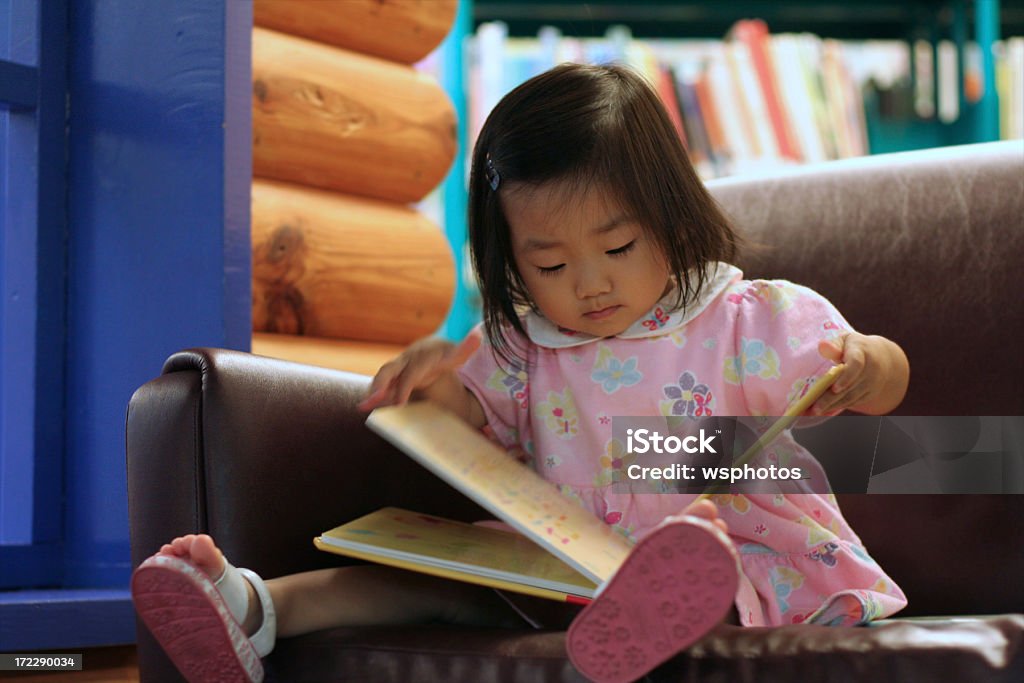 かわいいアジアの幼児の女の子の読書は保育園ライブラリー - 2歳から3歳のロイヤリティフリーストックフォト
