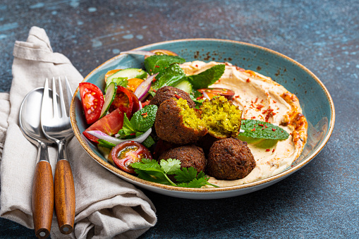 Close up of Middle Eastern Arab meal with fried falafel, hummus, vegetables salad with fresh green cilantro and mint leaves on ceramic plate on stone rustic background table. Arabic traditional cuisine