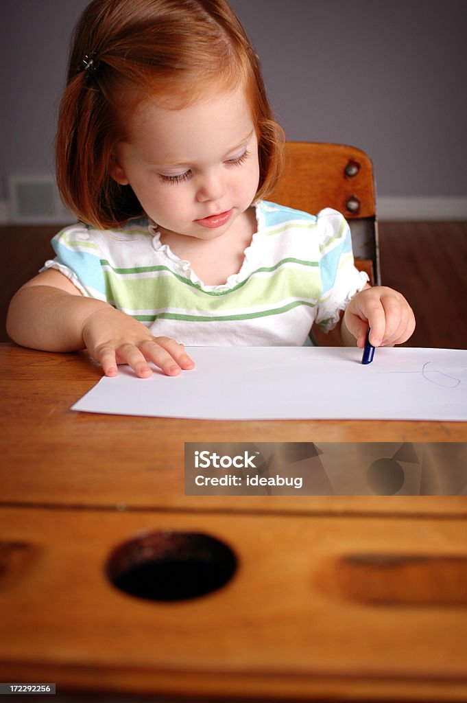 Learning to Write Little 22 month old girl writing on paper with a crayon in a school desk. Paper Stock Photo