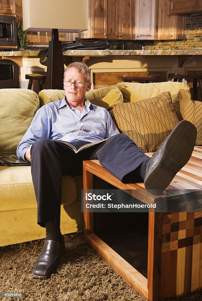 Uomo anziano rilassante sul divano e la lettura di una rivista - Foto stock royalty-free di Piedi alzati