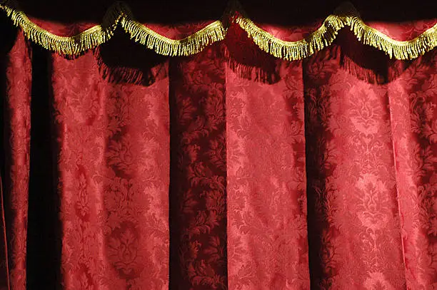 Photo of Close-up of a theater's red curtain with gold accents