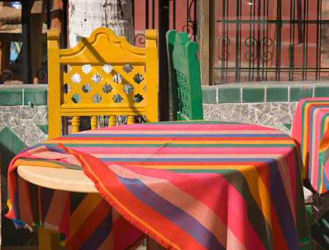 Horizontal close-up view of tables with brightly colored tablecloth and chairs in a casual Mexican restaurant outdoor cafe in Puerto Vallarta, Mexico.