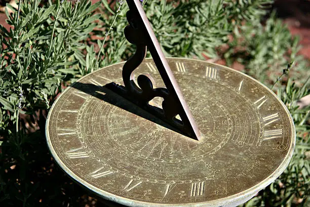 "An old ornamental sundial casts a short shadow on the face, in a garden setting."
