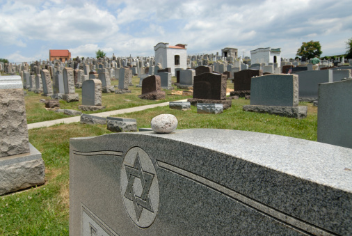 Scene at a Jewish cemetery with focus on stones left on headstone. It is a Jewish tradition for a visitor to a Jewish grade site to place a single stone on the monument. It tells visitors that follow that others have also visited this grave. A religious explanation is that stones are added to symbolize that we are never finished building a monument to the deceased.