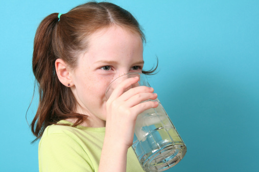 Eight year old girl drinking a glass of ice water on a blue background