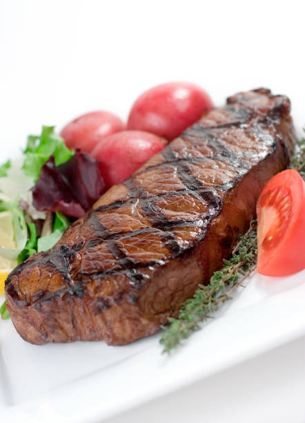 Grilled beef steak on a plate and a cup of salad on a wooden cutting board. Closeup.