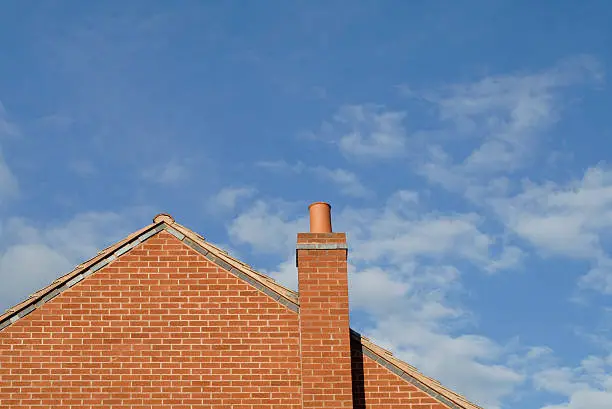 "Gable end of a modern brick house, with chimney and blue sky behind. Space for copy."