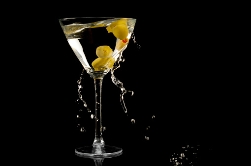 Martini with green olives, ice and lemon peel. Cocktail with splashes on a blue background.