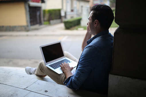 Young handsome freelancer sitting at street free time with new modern laptop