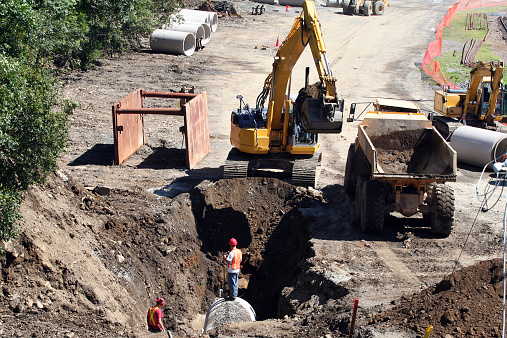Construction site crew with equipment lay a concrete pipe line under the ground.