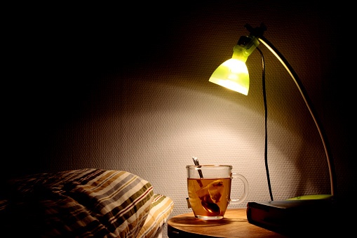 Bedside table with lamp, book and a cup of tea. Going to bed concept.