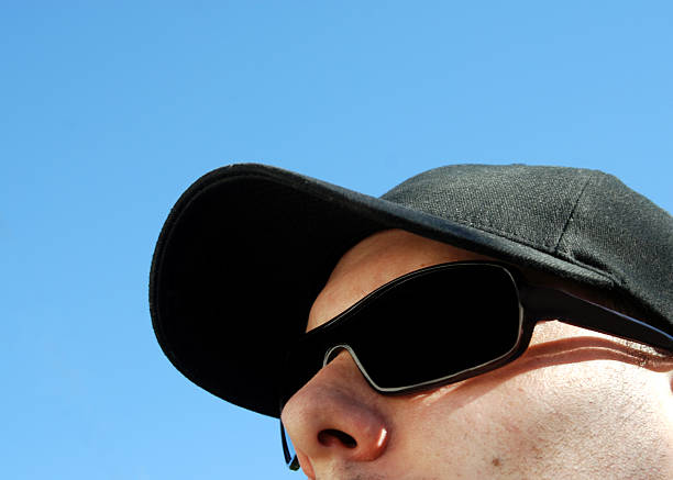 A man wears a black hat and sunglasses on a bright summer day. 