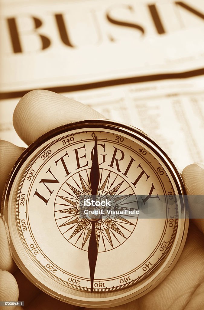 Compass Pointing the Way to Integrity in Business "Hand holding compass with needle pointing to INTEGRITY, with Business section of newspaper in background" Morality Stock Photo