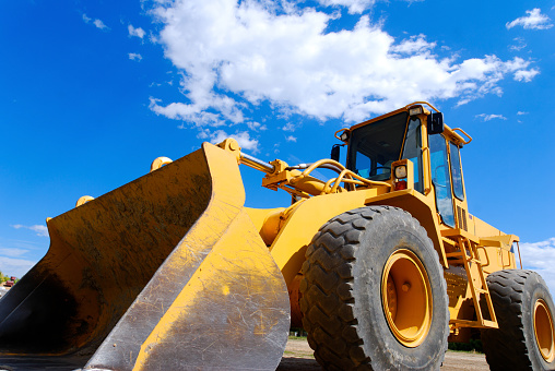 A yellow orange front end loader with a perfect blue sky background.
