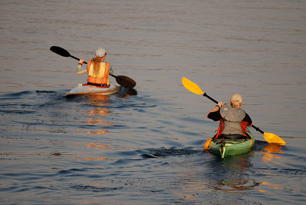 Two paddlers play in their kayaks on Great Slave Lake, Yellowknife Bay, Northwest Territories.  The lake is calm and it is twilight time.