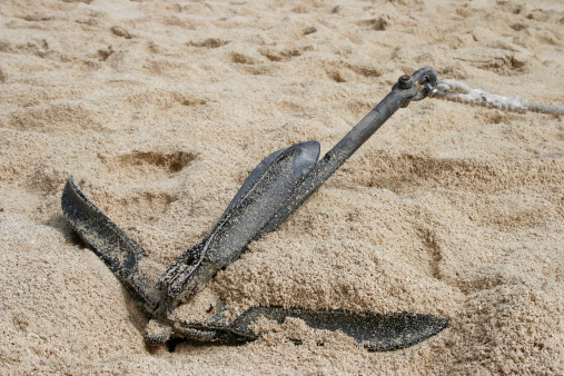 An anchor sitting in the sand of a beautiful beach.