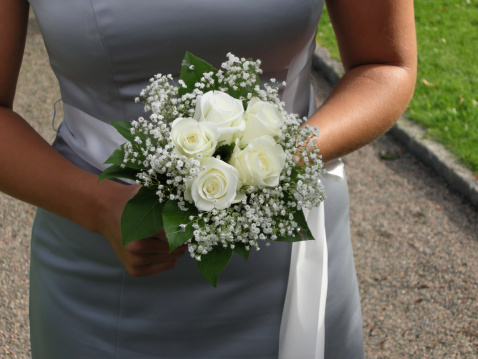 A closeup shot of a bride holding a white green bouquet with a hand with a wedding ring
