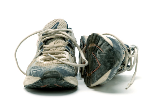 A pair of old, well-used running shoes, all logos and brand markings removed, shot on studio white
