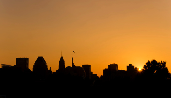 the sun sets behind a city skyline silhouette