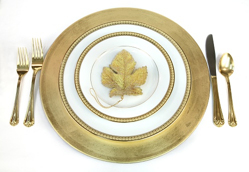 Gold and white place setting with beaded gold leaf decoration in center of plate. All on white background.  Horizontal image.