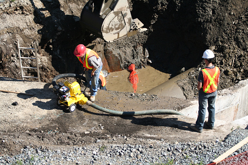 Construction site worker prepares to start a pump while supervisor looks on.