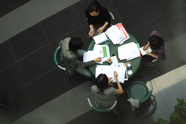 A casual business meeting between 1 man and 3 woman shot from above. Facial features and paperwork has been altered to protect the innocent.New to iStockphoto Click the badge below to sign up now: