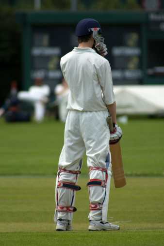 A batsman standing in the middle of the wicket with the scoreboard in the background