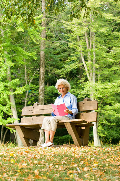 istock Elderly Woman Sitting On A Park Bench Reading 172317577