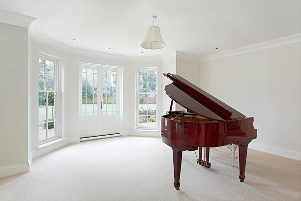 grand piano and living room a spacious living room in a luxury home with a grand piano sitting to the right. This room is unfurnished apart from the piano and the stool behind it. A large bay window area is in the background with beautifully crafted white wooden Georgian windows and French doors with views over a frosty garden scene. This image has been taken as a relatively high key image but with a nicely contrasting and colourful piano dominating in the foreground.Looking for a Living Room image Then please see my other Living Room and related images by clicking on the Lightbox link below... expensive grand piano stock pictures, royalty-free photos & images