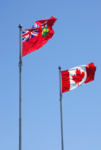 Province of Ontario and Canada flags under clear blue skies.