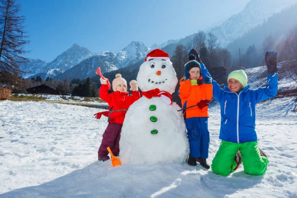 istock Three children play with snowman lift hands stand over mountains 1723183113