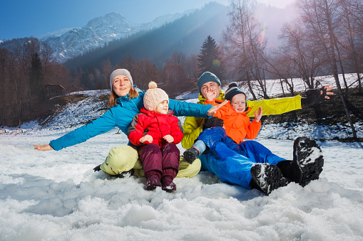 Family with two children mom dad have fun in snow hug sit over alpine landscape