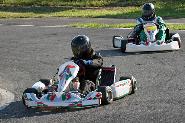istock Two people with helmets racing go-carts around a track 172318354