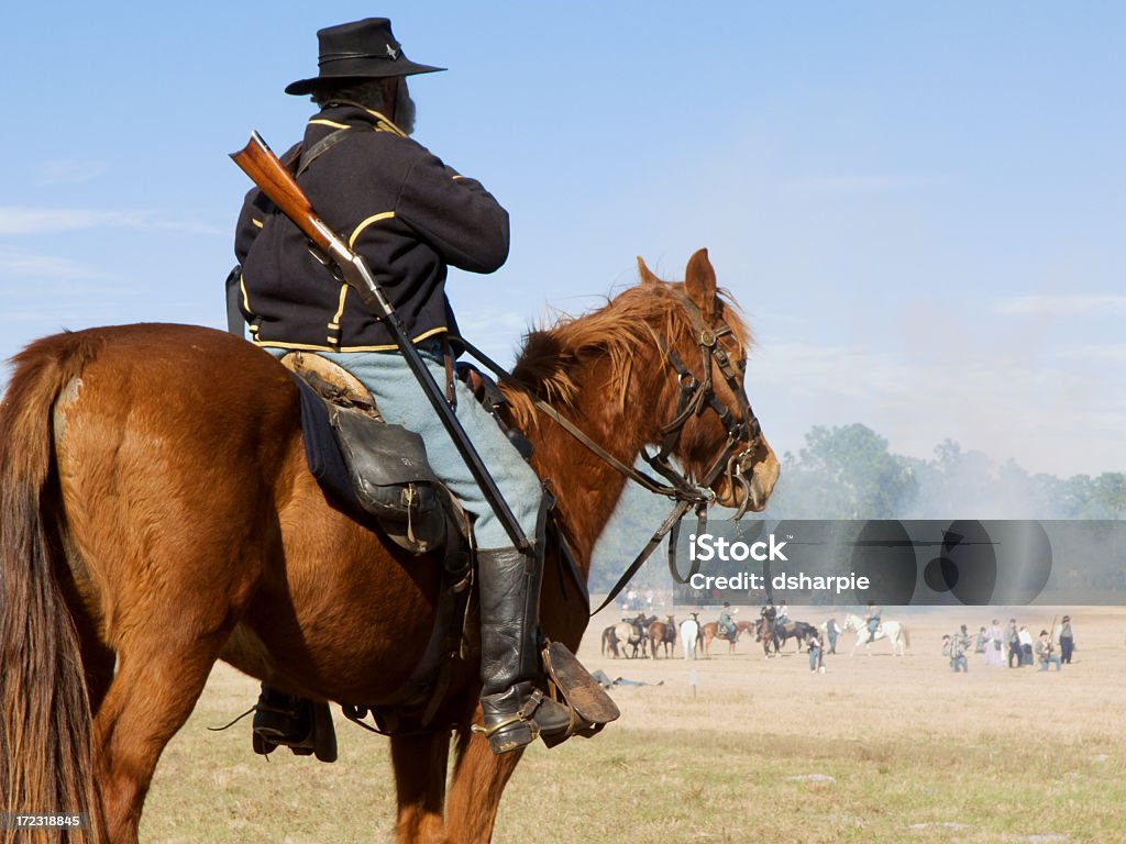 Civil War Reenactment - Union Cavalryman on Horse Federal (Union Army) calvaryman on horse depicted in a civil war reenactment. In the distant background, Rebel troops are preparing an attack while smoke hovers over the battleground. American Civil War Stock Photo