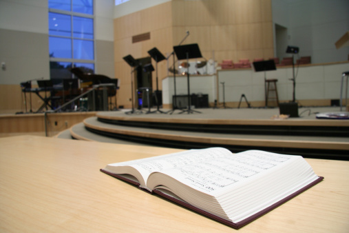 An open hymnal in front of a church's stage. Focus is on the hymnal page. 