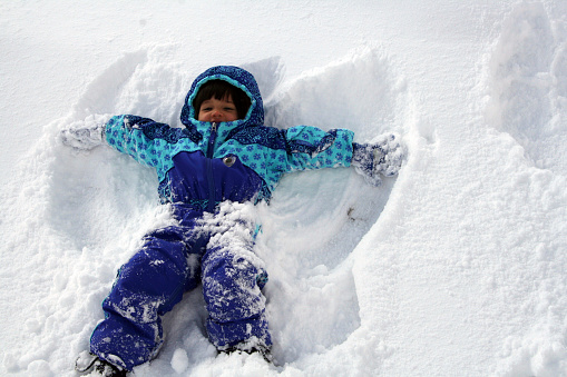 a young childing having fun making snow angels.