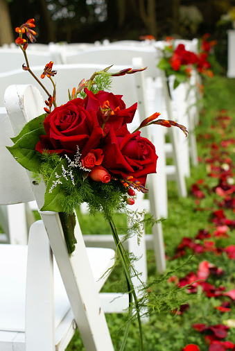 Bouquets and rose petals decorate the aisle at an outdoor wedding.  