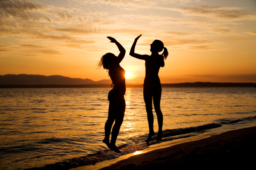 Silhouette of two girls high fiving on the beach at sunset.