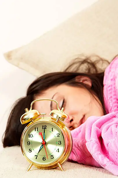 Closeup of golden alarm clock with beautiful girl sleeping in background (focus on clock)